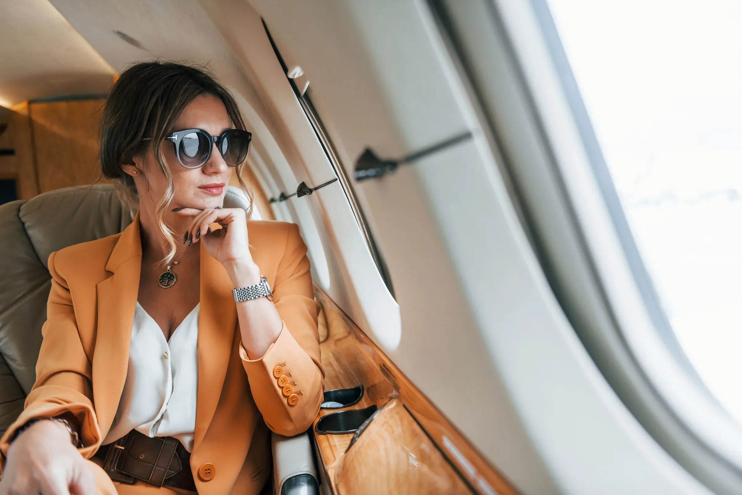 A woman in sunglasses resting against an aeroplane window in warm daylight.