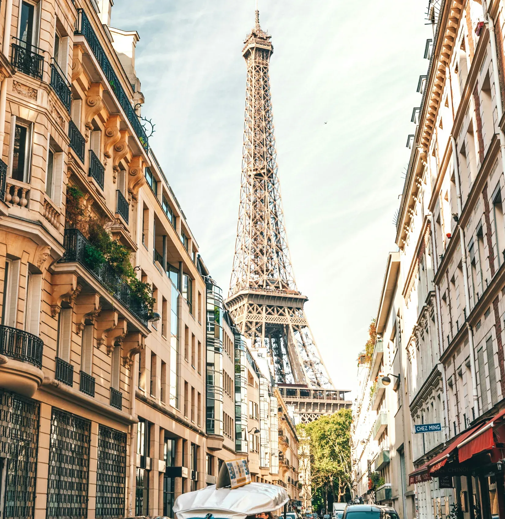 The Eiffel Tower seen upward between Haussmann façades.
