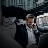 An image with a man talking to a phone in the back of the car, representing globally mobile people.