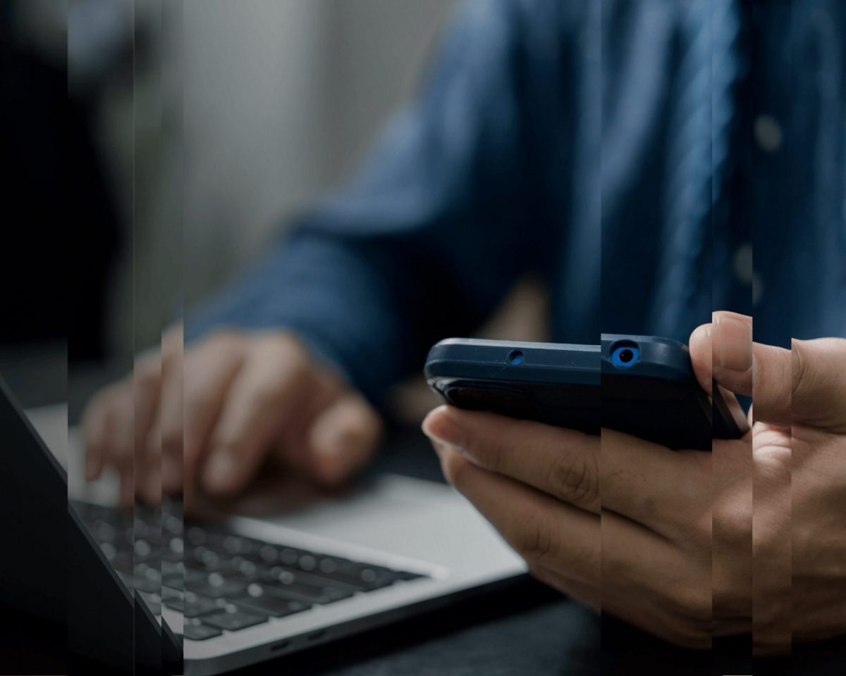 A picture of a man holding a mobile phone and on a laptop, symbolising the modernisation of trust compliance.